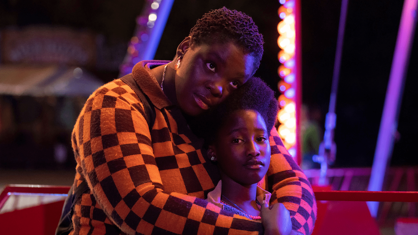 A mother holds a child close as neon lights dance over their faces - the mother is wearing a vibrant patterned shirt.